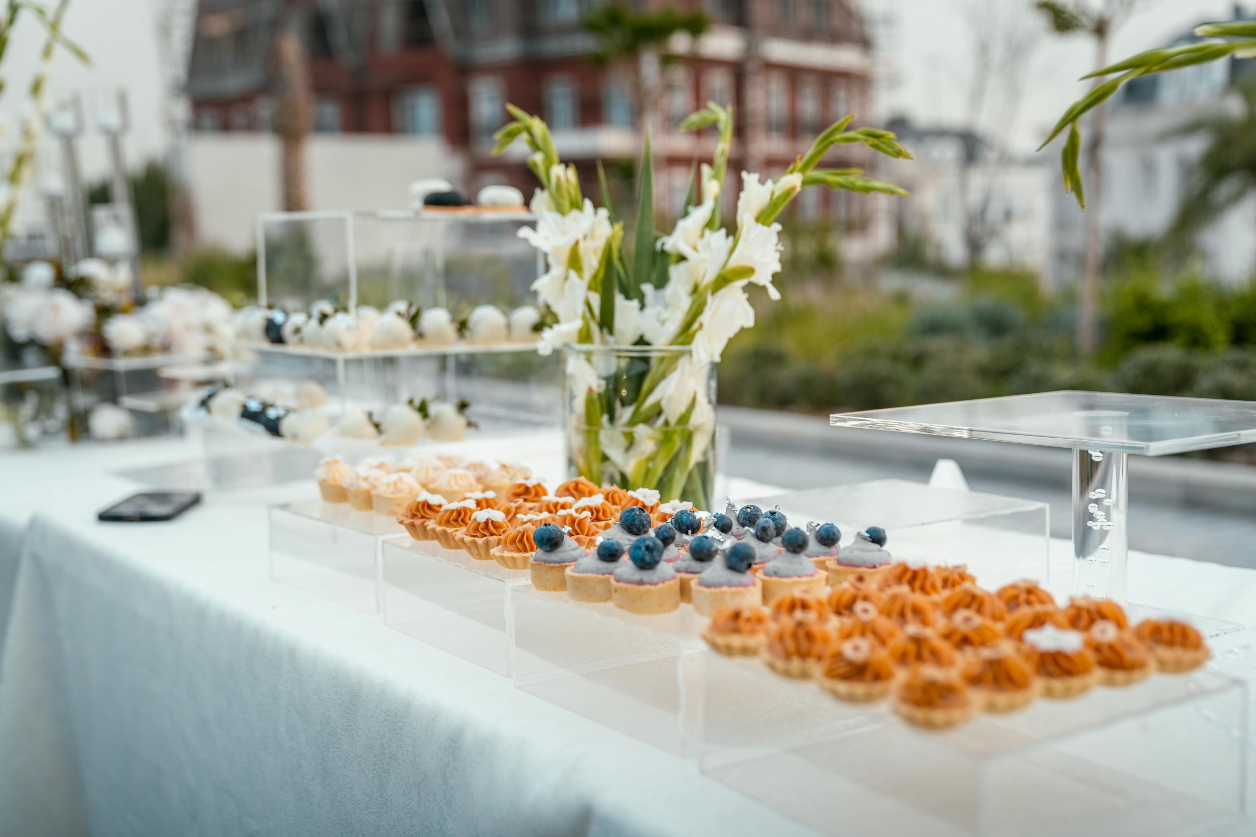 Beautiful arrangement of desserts and flowers on a table outdoors, perfect for events and celebrations.
