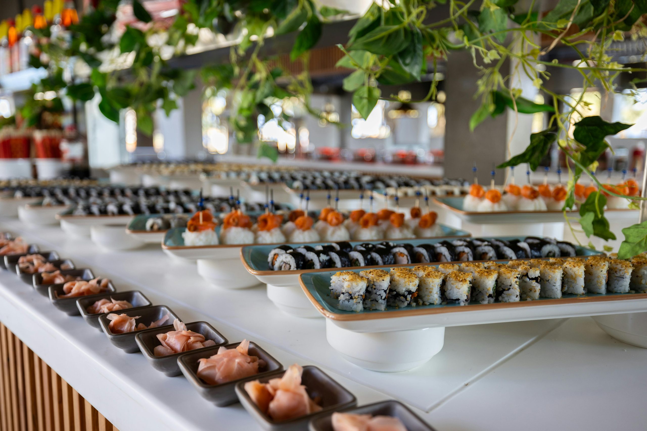 A delightful assortment of sushi rolls elegantly displayed at a buffet, garnished with pickled ginger and surrounded by lush greenery.